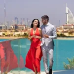 Couple in Dubai, man in pent coat and girl in red glamour dress on boat in Dubai near blue sea water enjoying Dubai Lifestyle